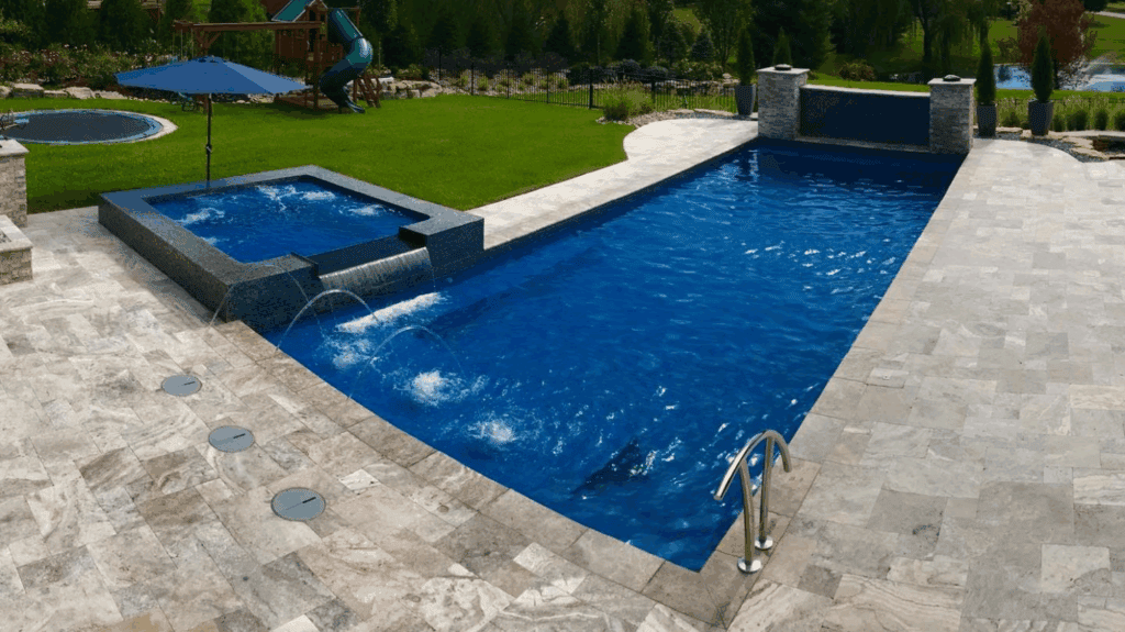 Modern backyard pool with spa, water slide, and lush landscaping.